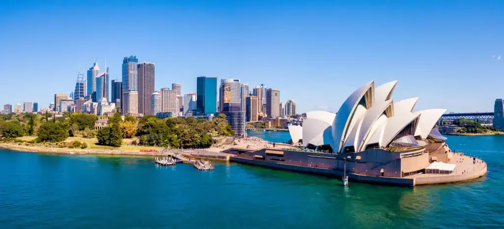 Aerial view of Sydney Opera House with its iconic white shell-shaped roof, Sydney Harbour, and the CBD skyline under a clear blue sky